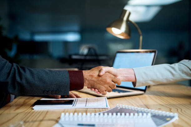 Closeup shot of two businesspeople shaking hands in an office at night